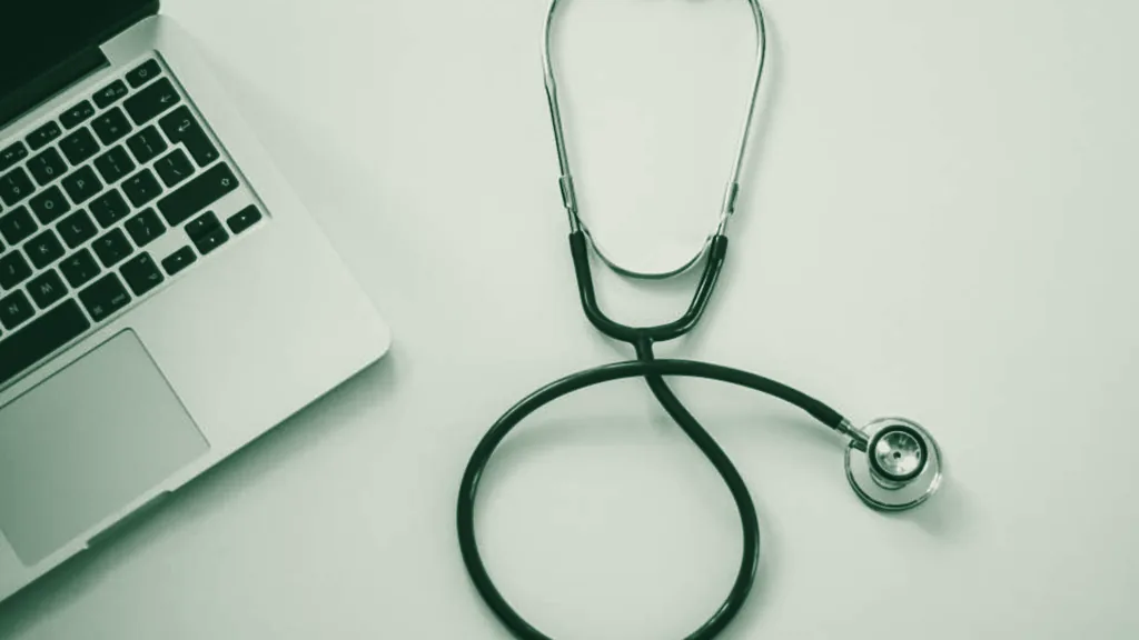 A stethoscope beside a laptop, toned in green